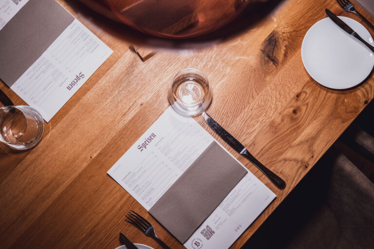 Tisch mit Wasser, Menükarten, Besteck und leeren Tellern in einem Restaurant.