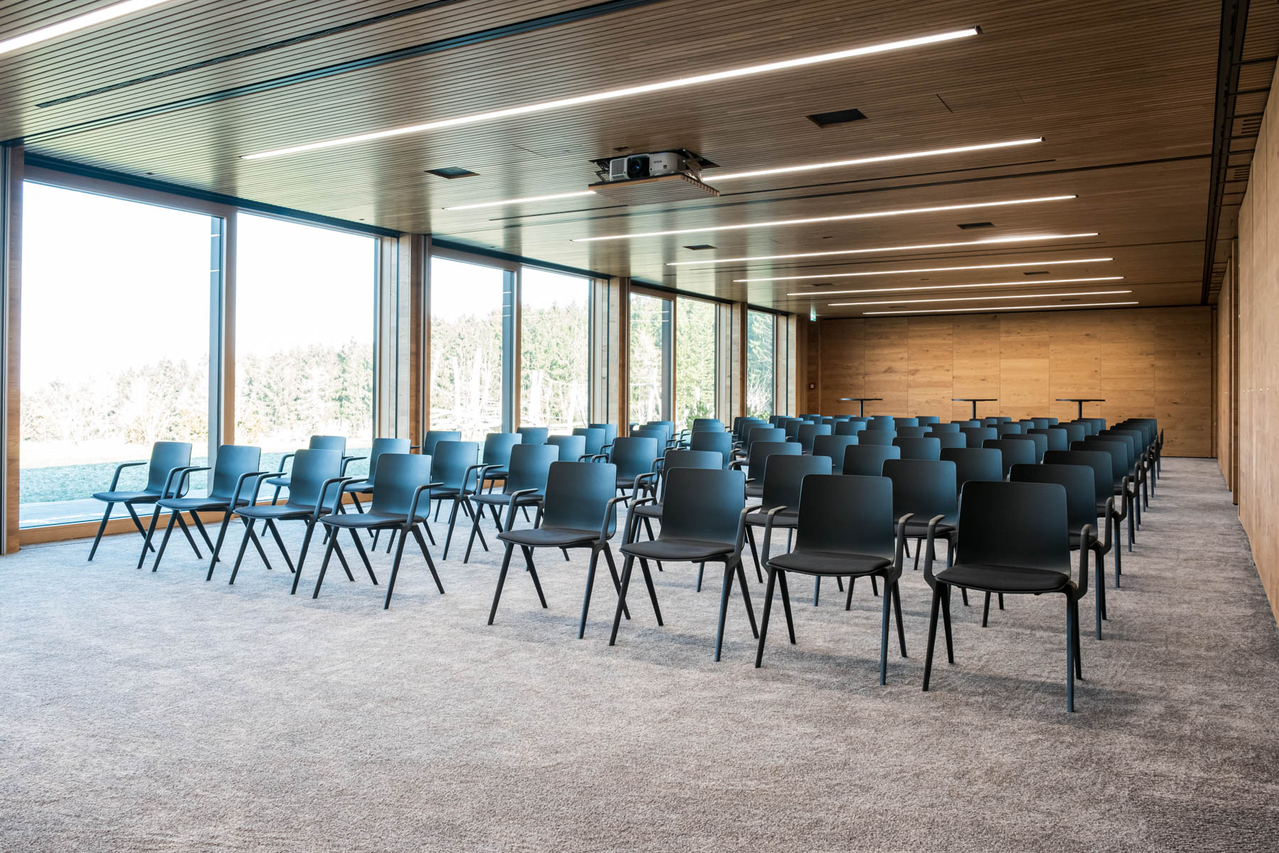 Moderne Konferenzraum mit Stühlen, Holzdecke und großen Fenstern, ideal für Meetings und Veranstaltungen.