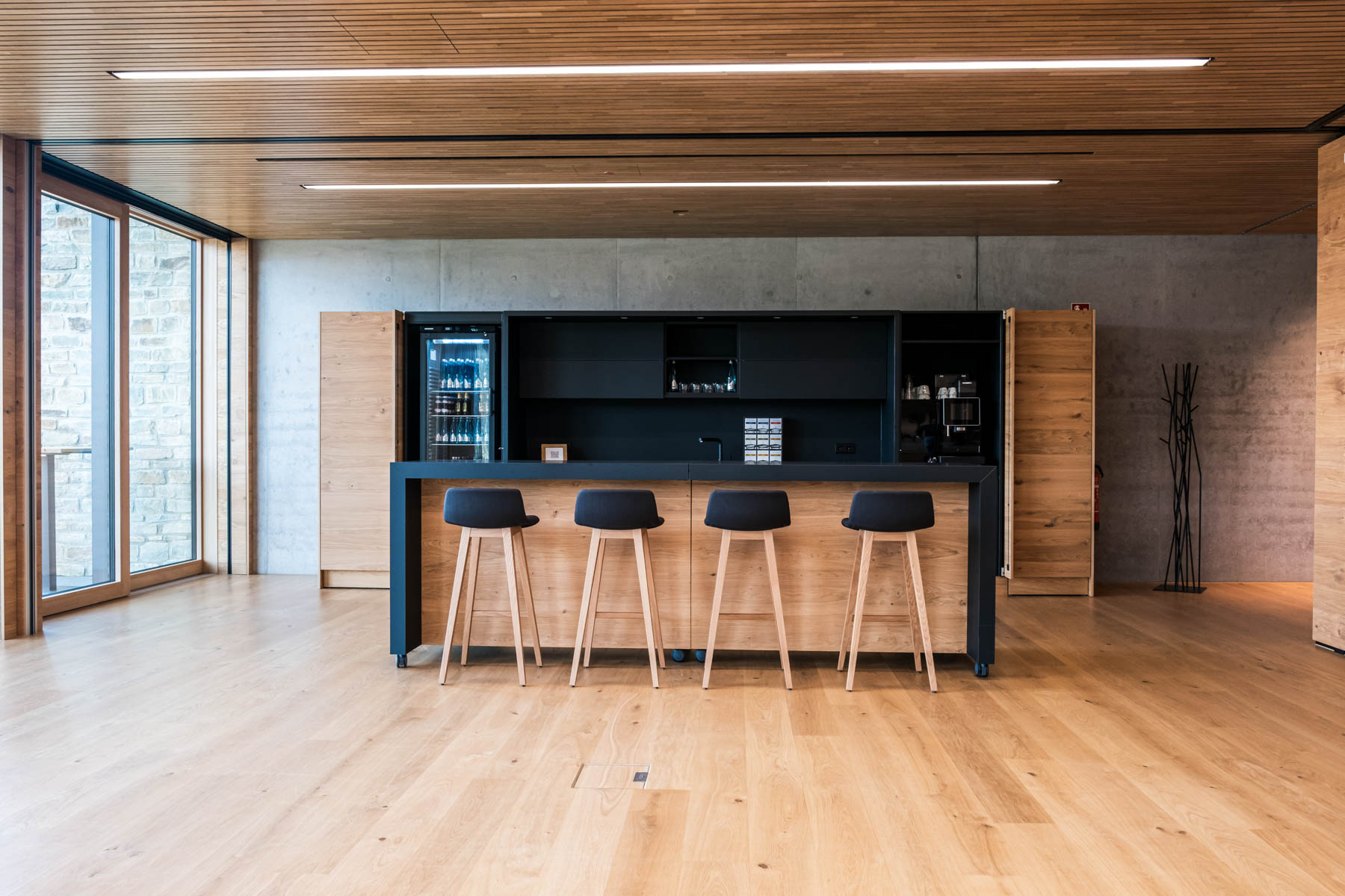 Moderner Bar im Holzdesign mit schwarzen Barhockern und Kühlschrank.