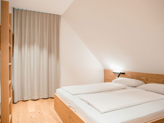 Modernes Schlafzimmer mit Doppelbett, Holzdekoration und Vorhängen.