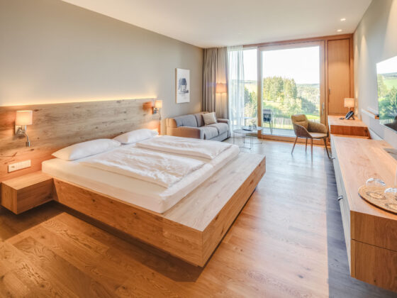Modernes Hotelzimmer mit Blick auf grüne Landschaft und Balkon, Holzdekor und gemütliche Einrichtung.