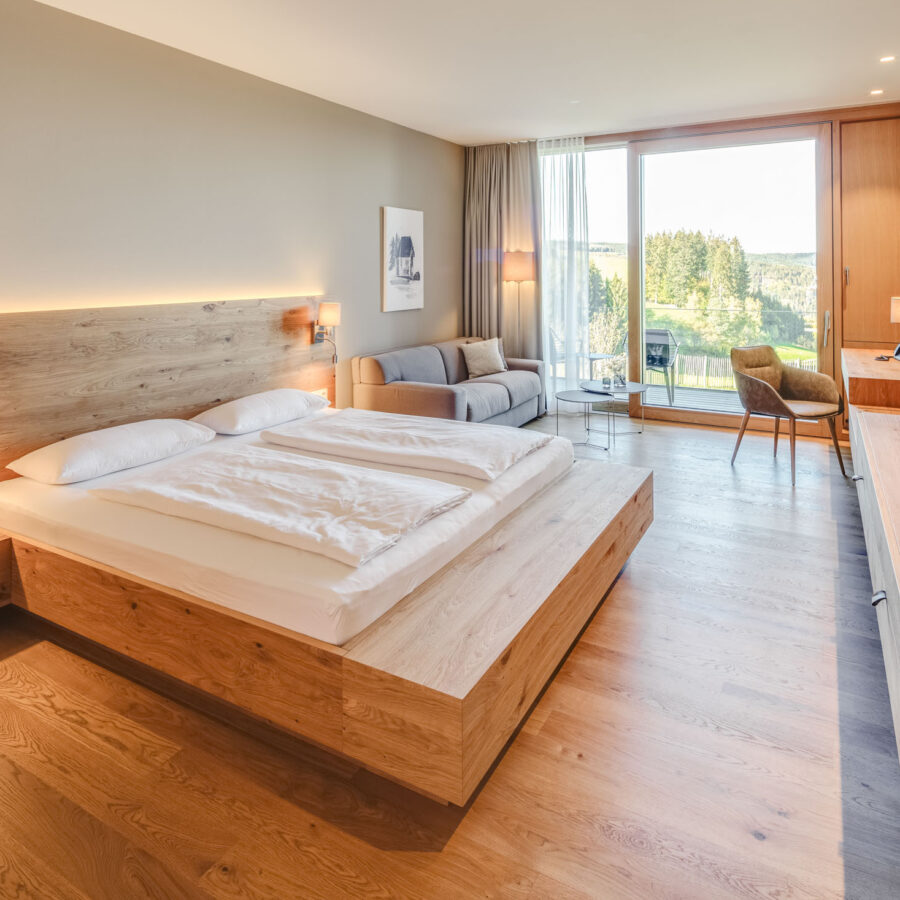 Modernes Hotelzimmer mit Blick auf grüne Landschaft und Balkon, Holzdekor und gemütliche Einrichtung.