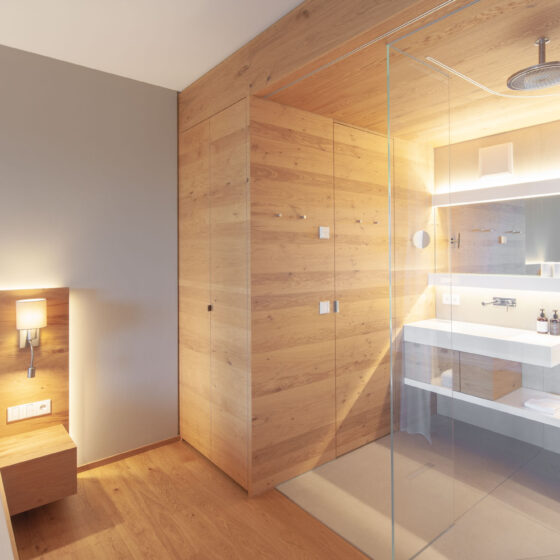 Modernes Hotelzimmer mit Holzdesign und offener Duschbereich mit Glaswand.