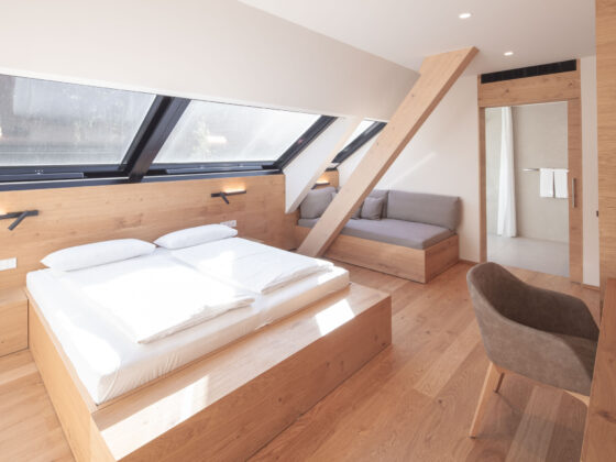 Modernes Hotelzimmer mit Doppelbett, Sitzbereich und Dachfenstern in Holzoptik.