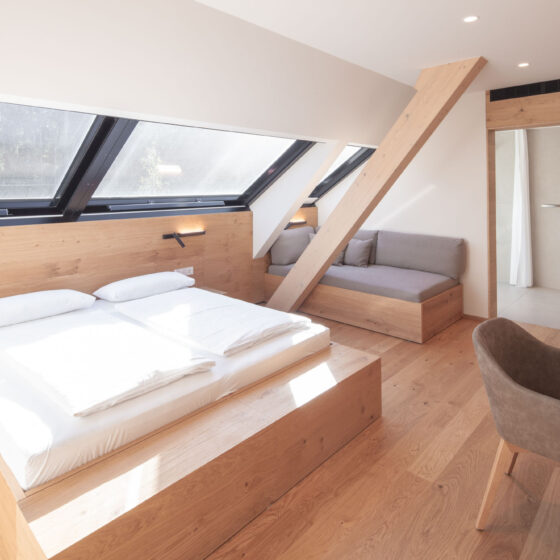Modernes Hotelzimmer mit Doppelbett, Sitzbereich und Dachfenstern in Holzoptik.