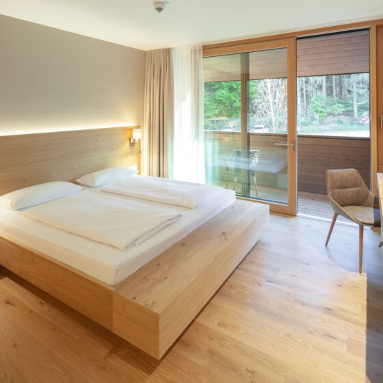 Modernes Hotelzimmer mit Doppelbett, Balkon und Naturblick in Holz-Design.