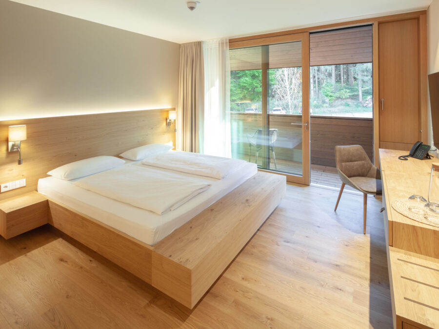 Modernes Hotelzimmer mit Doppelbett, Balkon und Naturblick in Holz-Design.