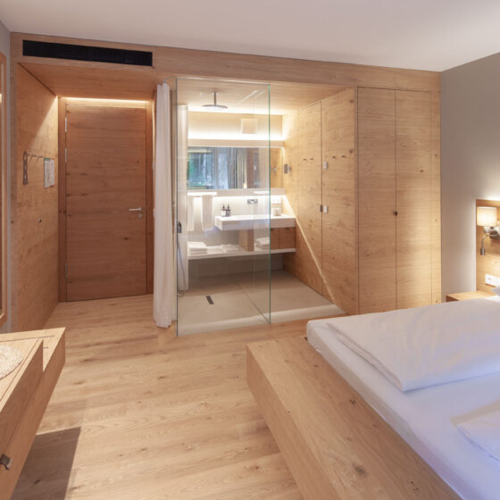 Modernes Hotelzimmer mit Holzdesign, offener Dusche und gemütlichem Bett.