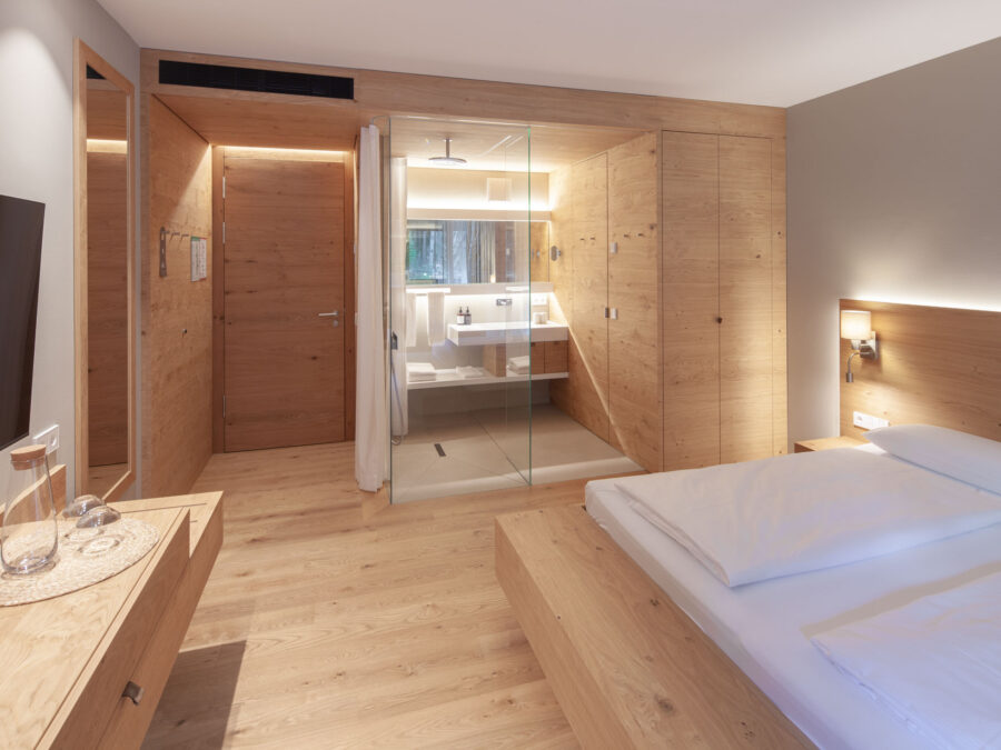 Modernes Hotelzimmer mit Holzdesign, offener Dusche und gemütlichem Bett.