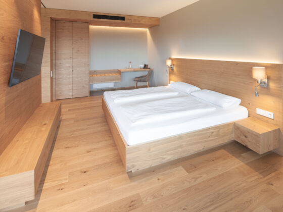 Modernes Hotelzimmer mit Holzdesign, Doppelbett, Wandlampen und TV.