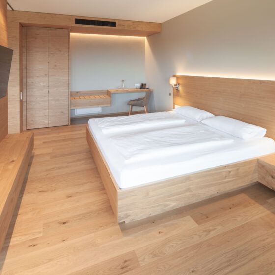 Modernes Hotelzimmer mit Holzdesign, Doppelbett, Wandlampen und TV.