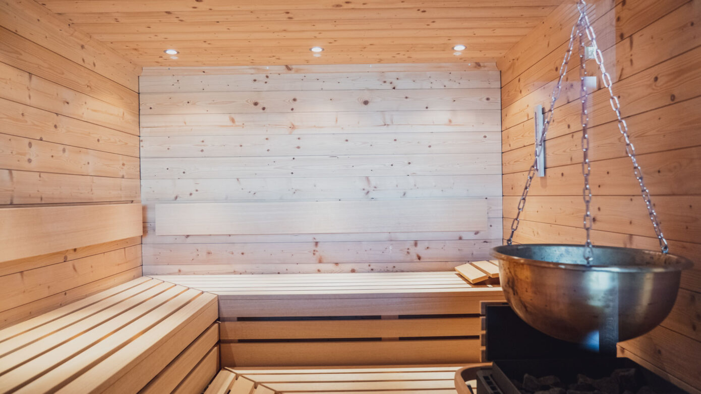 Innenansicht einer luxuriösen finnischen Sauna aus Holz mit Saunaofen und Liegen.
