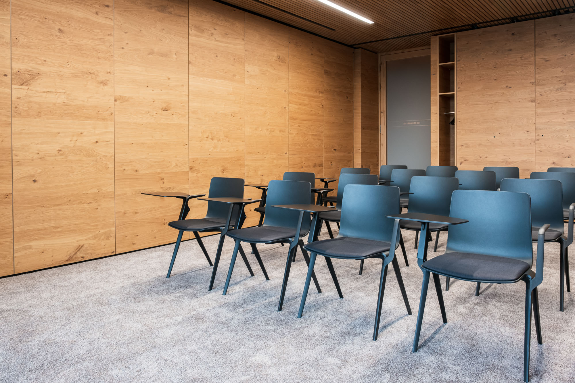 Leerer Seminarraum mit blauen Stühlen und Holzwand, ideal für Meetings und Schulungen.