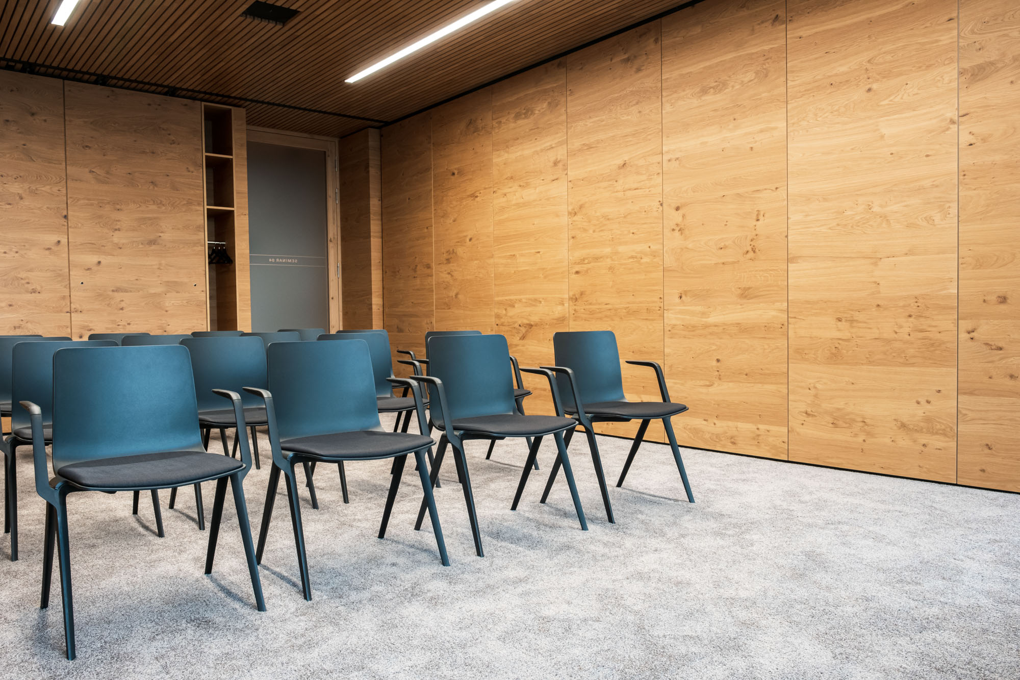 Leerer Konferenzraum mit blauen Stühlen, Holzpaneelen und moderner Beleuchtung.