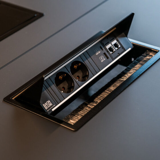 Hochwertige Steckdosenleiste mit USB-Ports und Kabelmanagement auf dunklem Tisch.