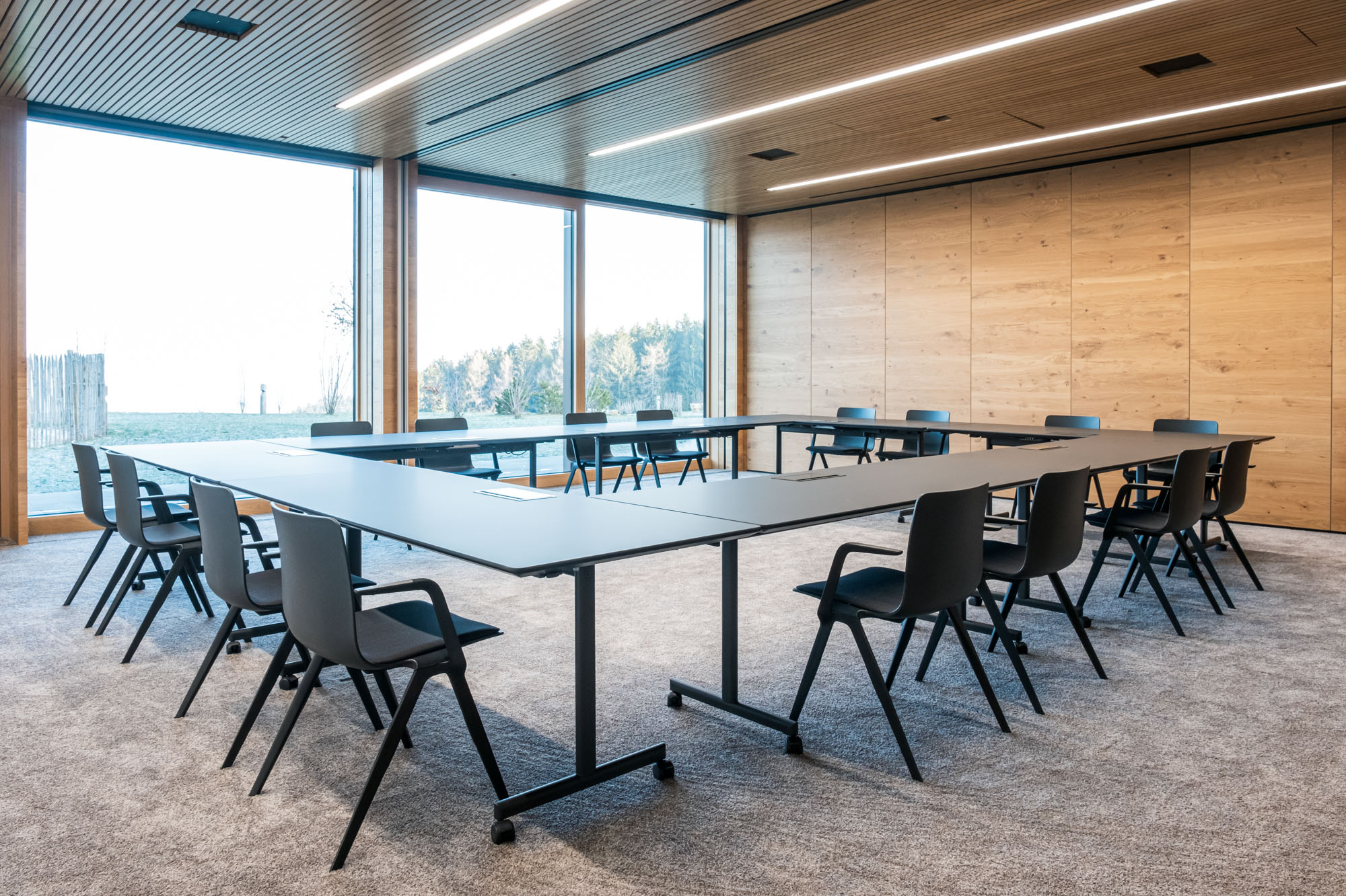 Moderner Konferenzraum mit großen Fenstern und schwarzen Stühlen.