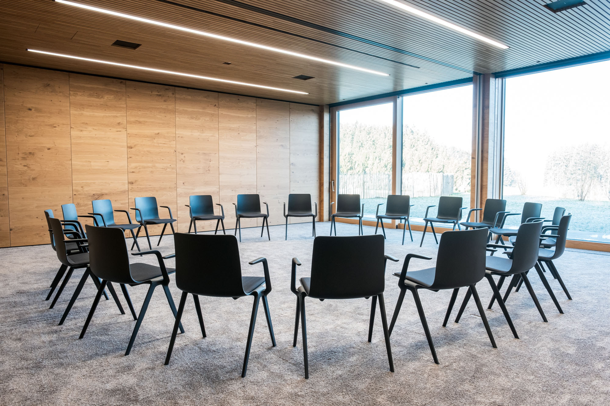 Leerer Sitzkreis in modernem Konferenzraum mit Holzdecke und großen Fenstern.