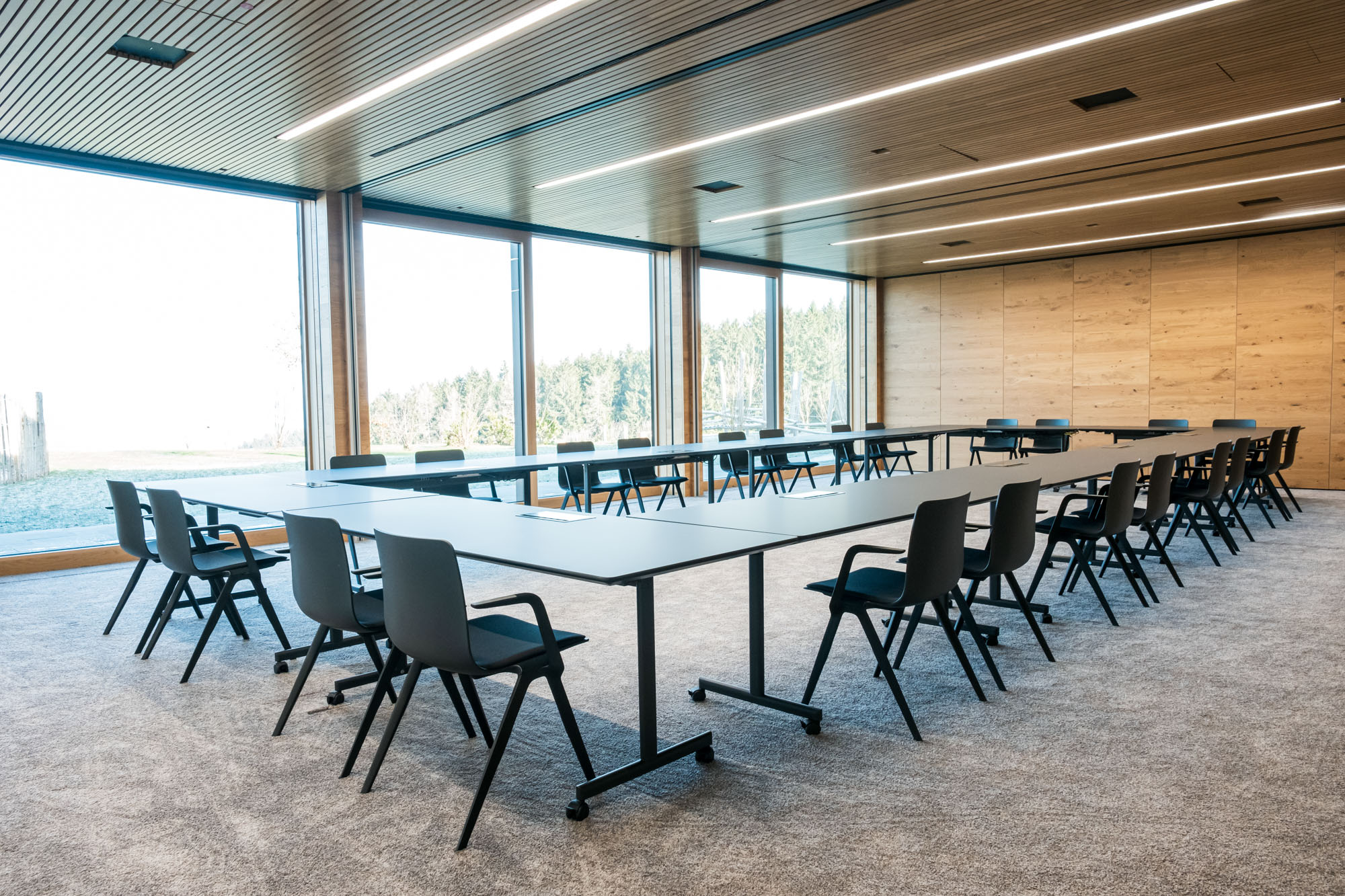 Moderne Konferenzraum mit Tischen, Stühlen und großen Fenstern, natürlicher Lichtquelle.