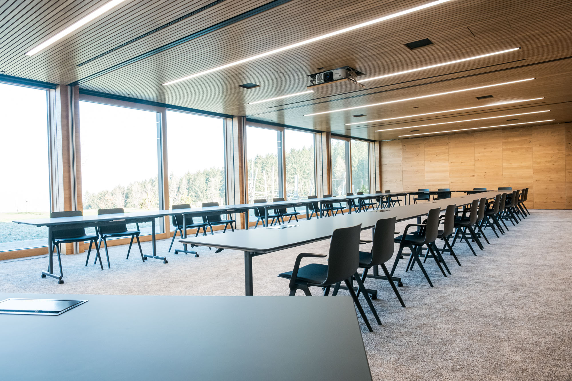 Moderne, helle Konferenzraum mit großen Fenstern, Tische und Stühle, ideal für Meetings.