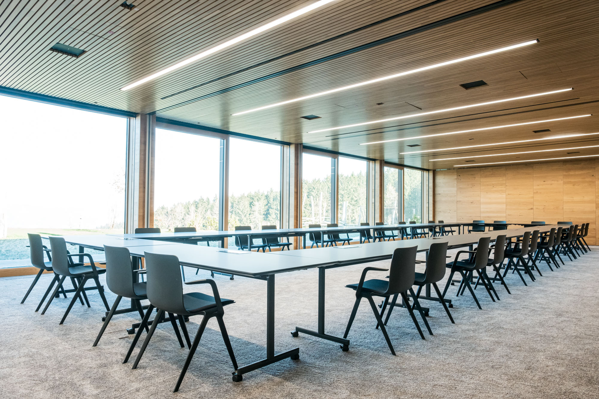 Moderne Konferenzraum mit großen Fenstern, Tischen und Stühlen.