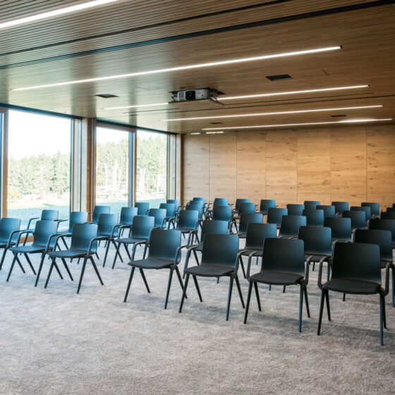 Moderne Konferenzraum mit schwarzen Stühlen, großen Fenstern und Holzdecke.