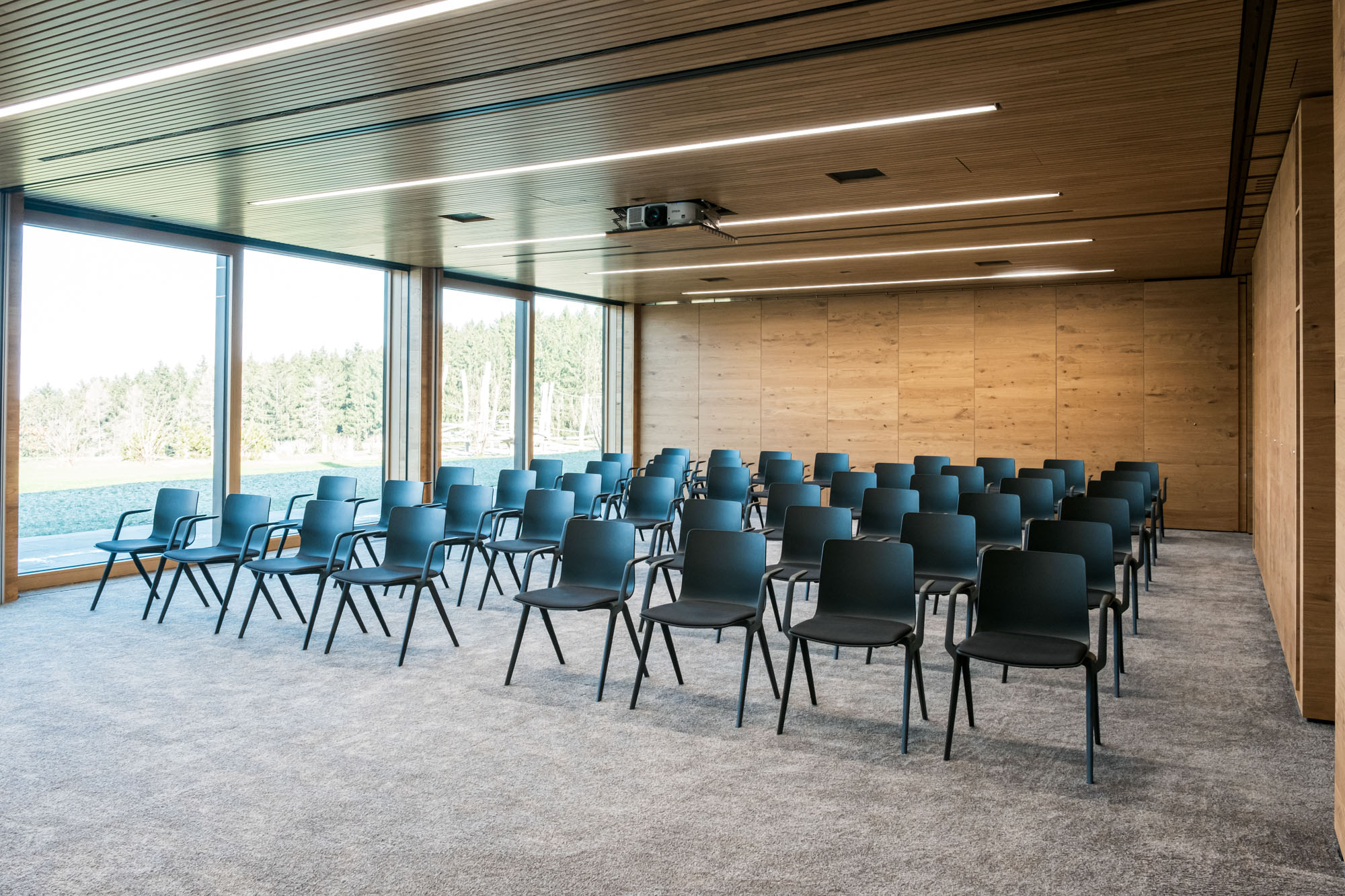 Moderne Konferenzraum mit schwarzen Stühlen, großen Fenstern und Holzdecke.