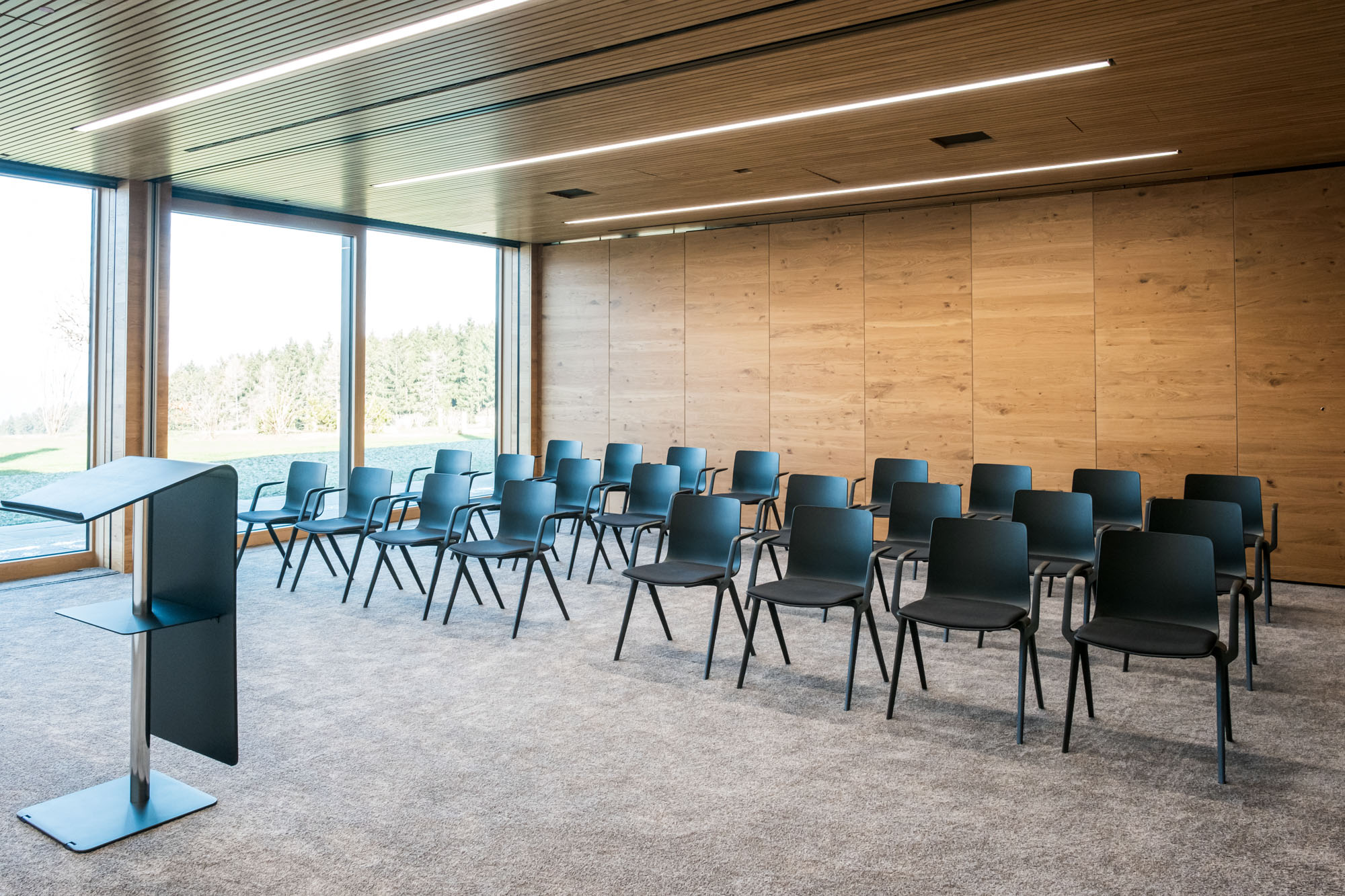 Moderne, leere Konferenzraum mit schwarzen Stühlen, Holz-Wand und großen Fenstern.