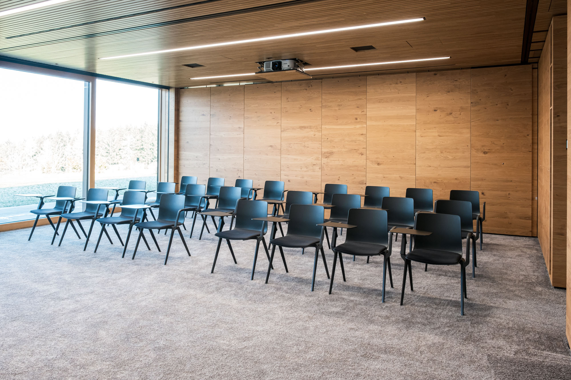 Leerer Konferenzraum mit schwarzen Stühlen und Holzwand, große Fenster, natürliche Beleuchtung.