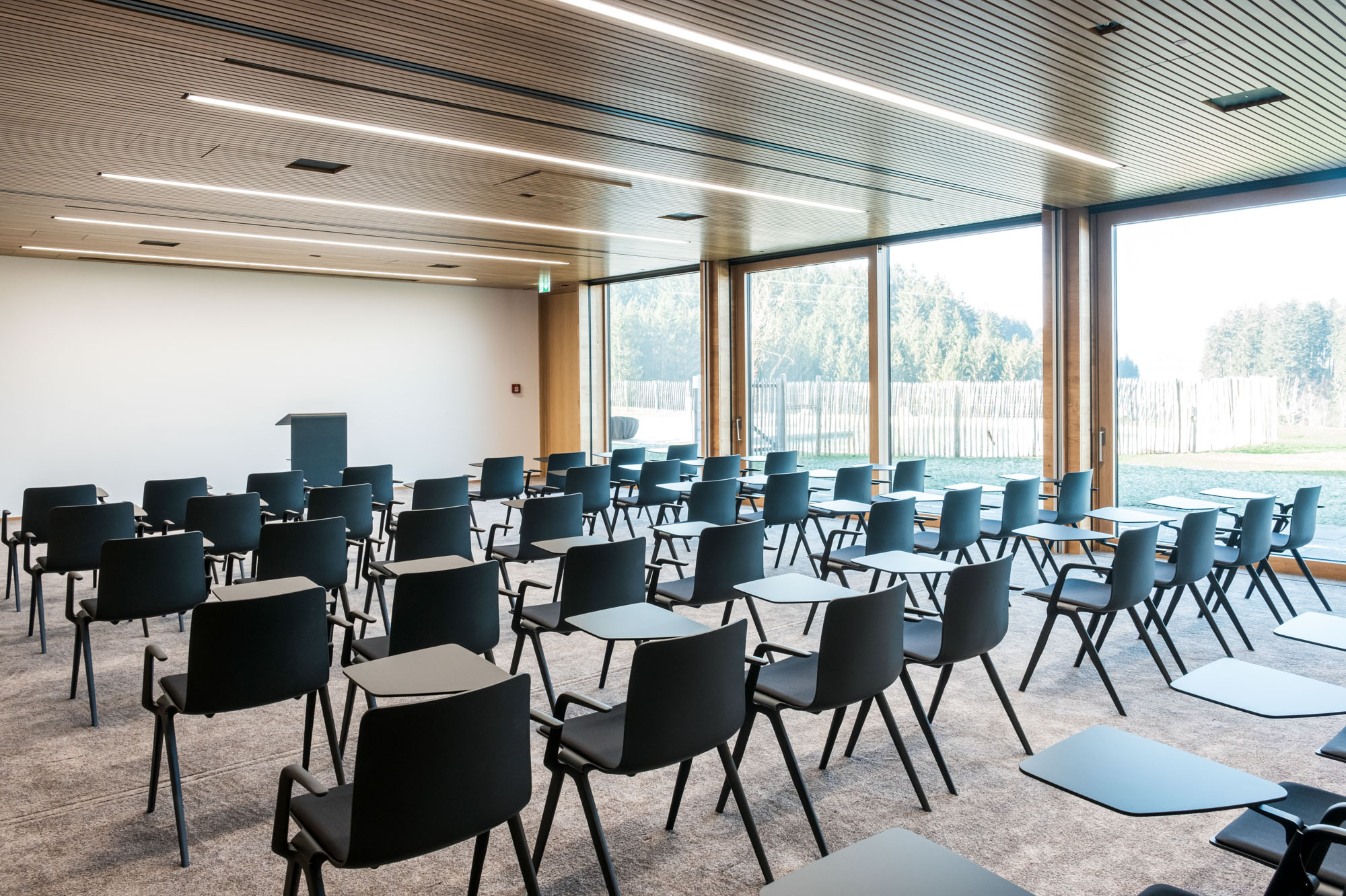 Moderne, leere Konferenzraum mit schwarzen Stühlen und großen Fenstern, viel Tageslicht.