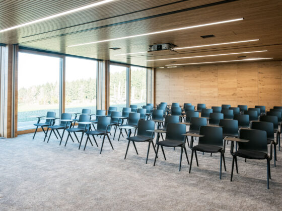 Moderne Konferenzraum mit schwarzen Stühlen, Holzdecke und großen Fensterfronten.