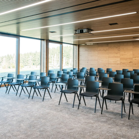 Moderne Konferenzraum mit schwarzen Stühlen, Holzdecke und großen Fensterfronten.