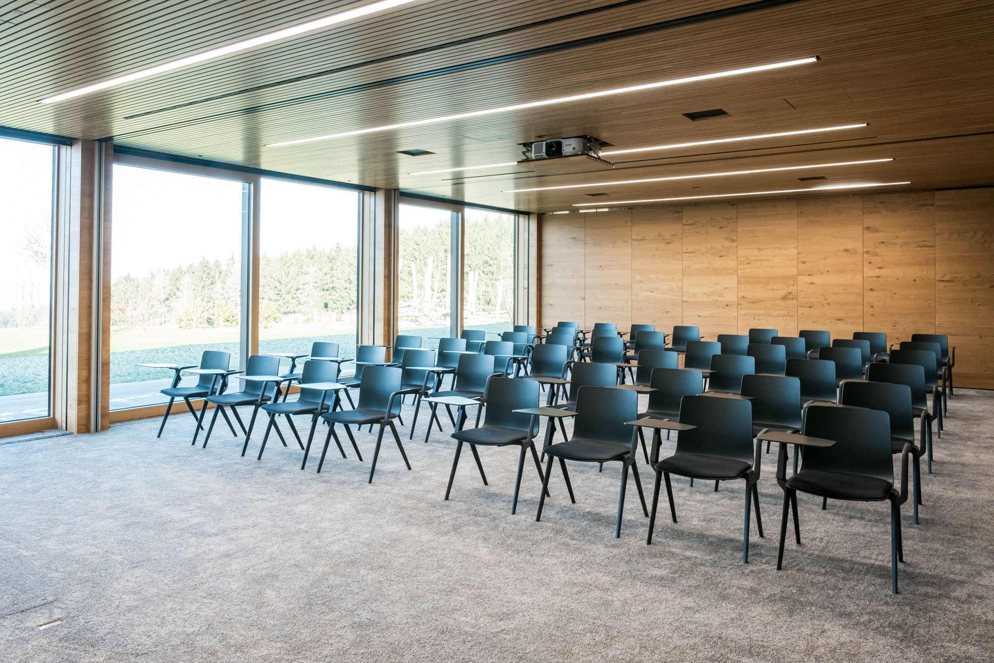 Moderne Konferenzraum mit schwarzen Stühlen, Holzdecke und großen Fensterfronten.