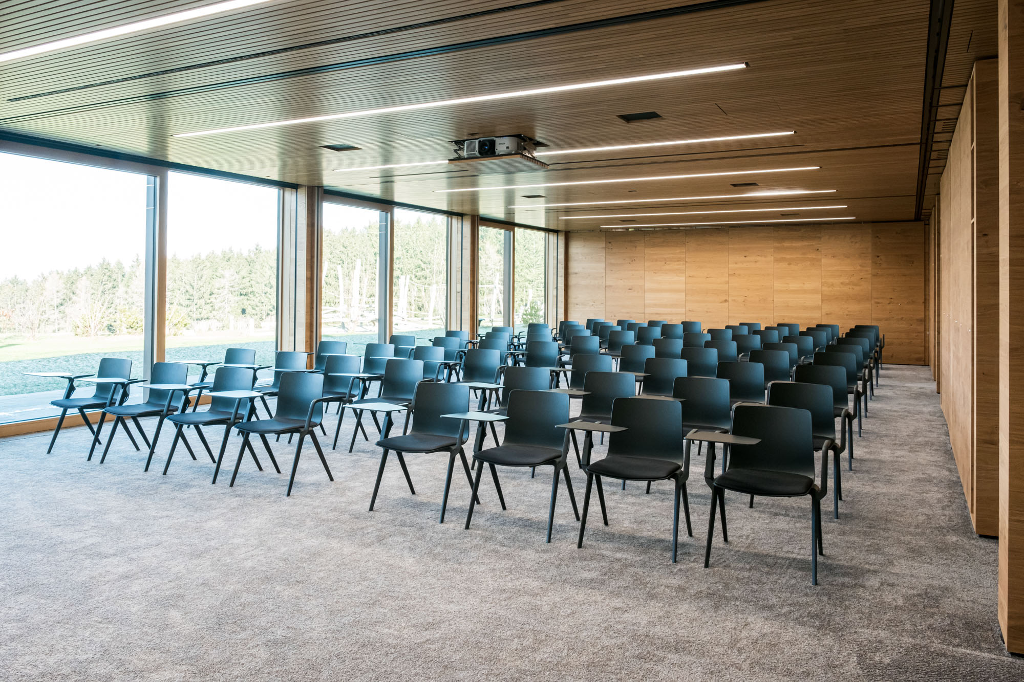 Moderner Konferenzraum mit schwarzen Stühlen und großen Fensterfronten, natürliche Holzelemente.
