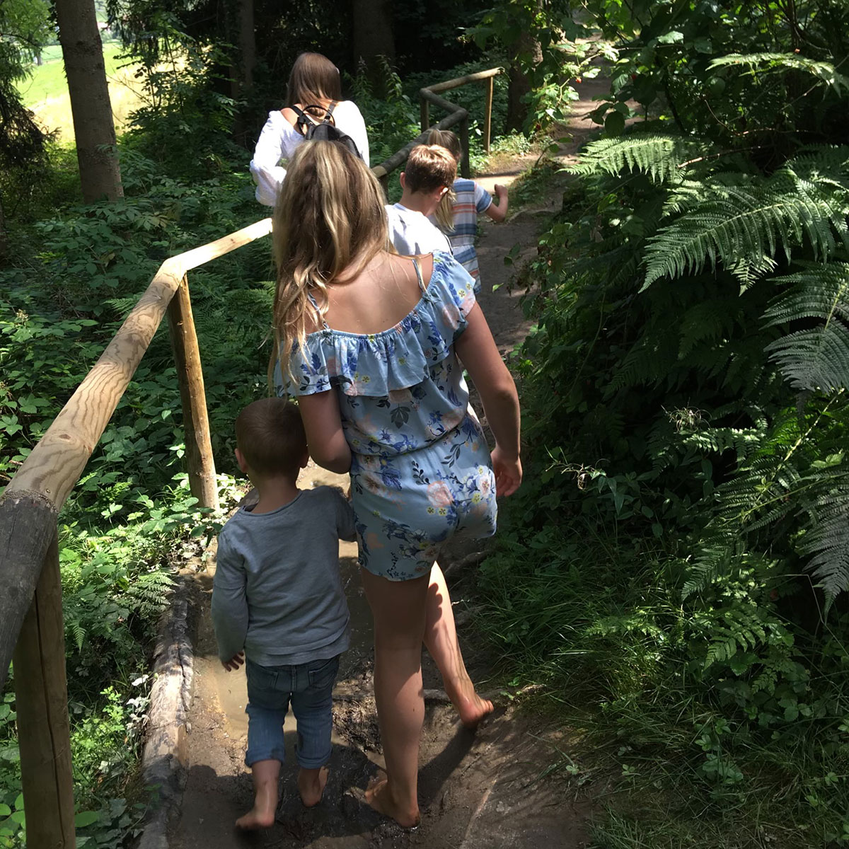 Familie beim Spaziergang im grünen Wald, barfuß auf einem schmalen Pfad.