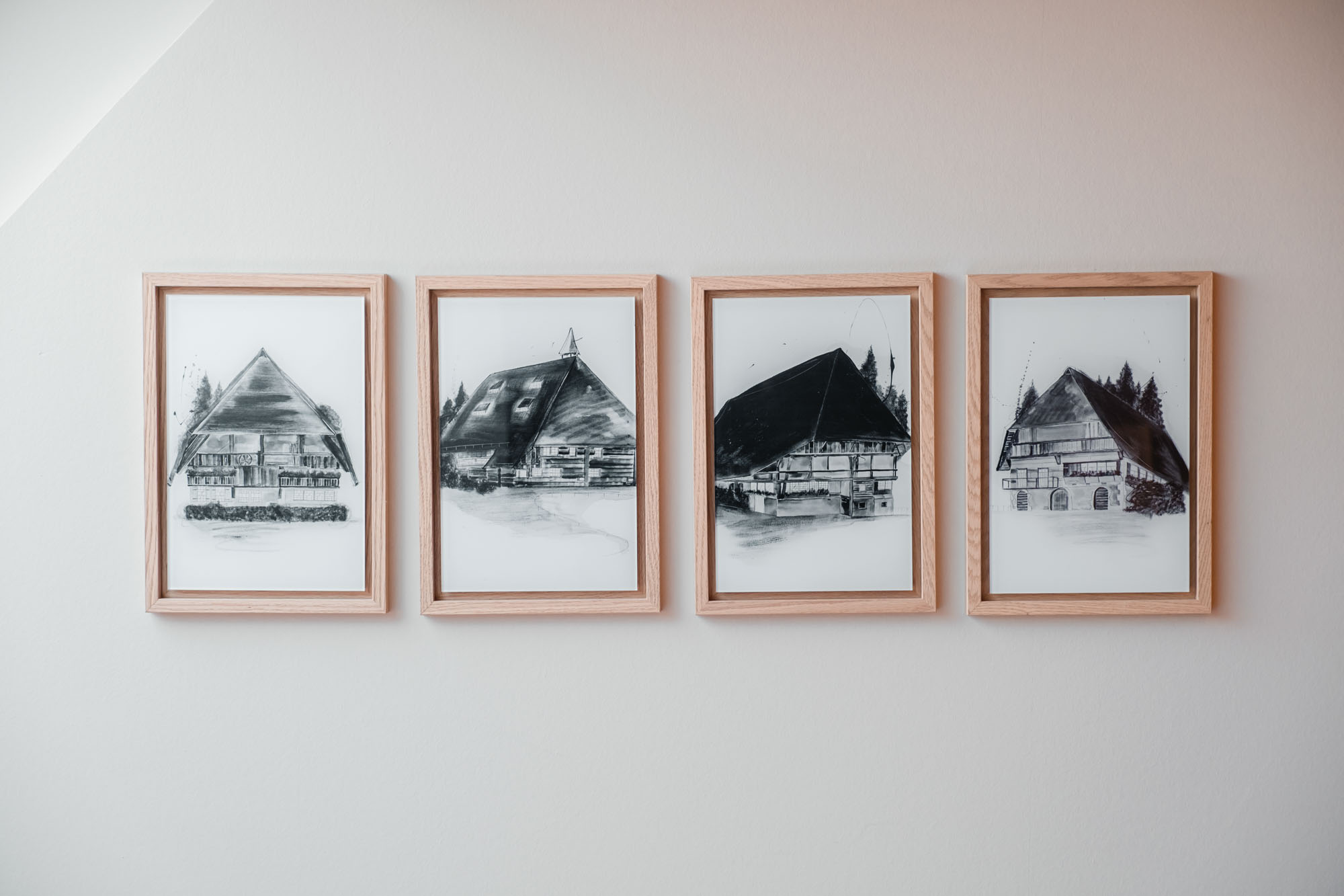 Vier Schwarz-Weiß-Bilder von traditionellen Häusern in Holzrahmen an weißer Wand.