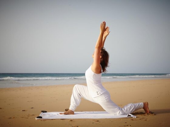 Frau macht Yoga im Sonnengruß auf dem Strand am Meer.