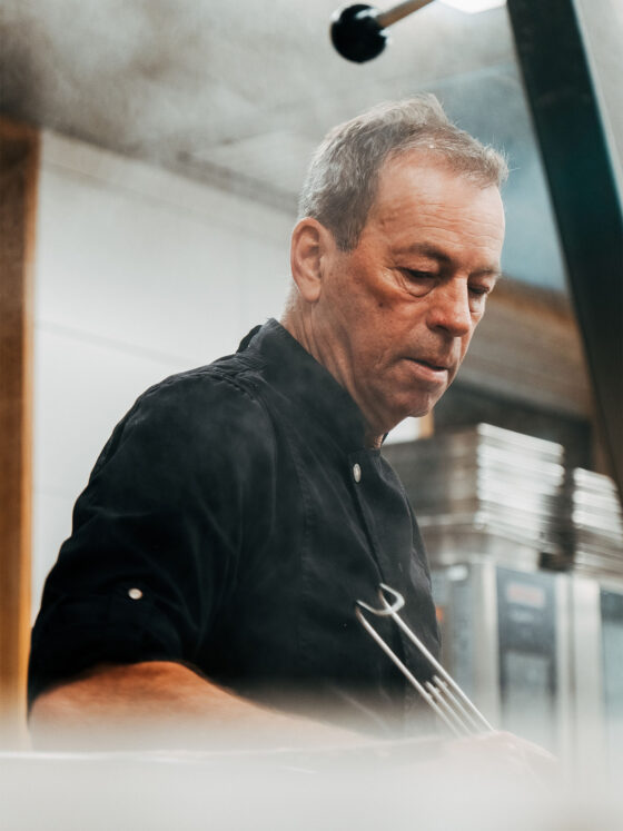 Koch in schwarzer Uniform beim Kochen in professioneller Küche.