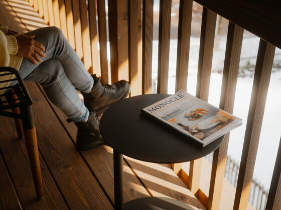 Person auf Balkon mit Zeitschrift "Monocle" und winterlichem Ausblick im Hintergrund.
